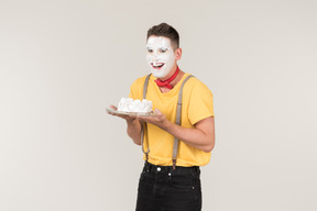 Male clown with cake cream on his face holding a cake