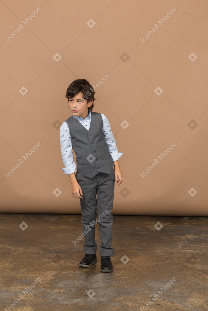 Vista frontal de um menino bonito de terno cinza olhando algo com interesse