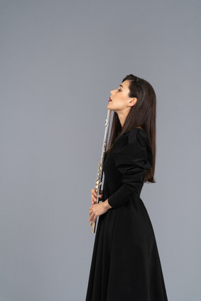 Side view of a serious young lady in black dress holding flute