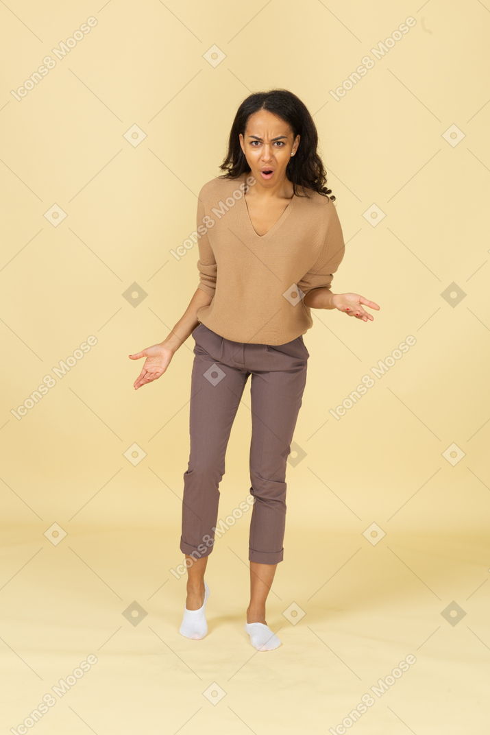 Front view of a questioning dark-skinned young female raising hand