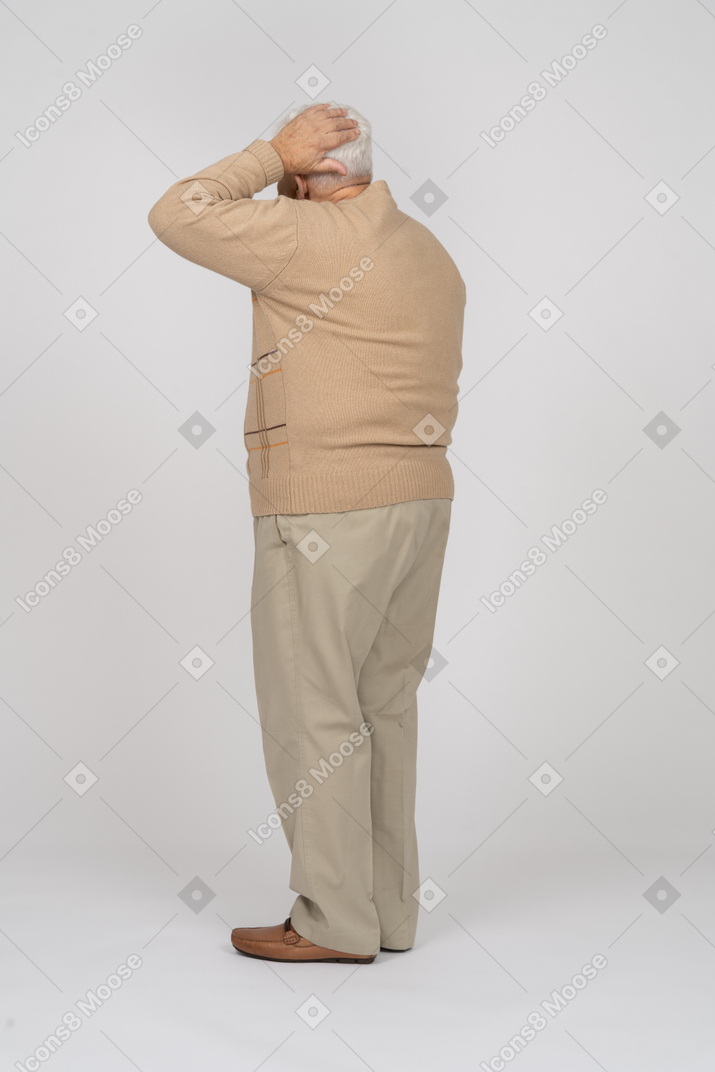Side view of an old man in casual clothes standing with hand on head