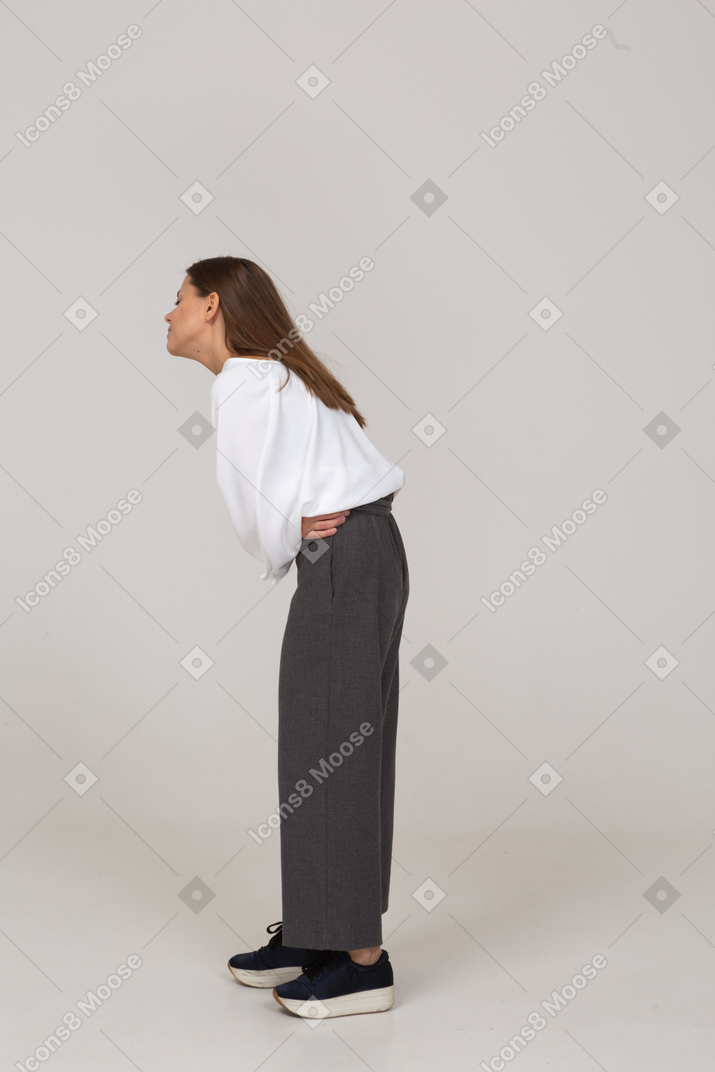 Side view of a young lady in office clothing with stomach ache bending down