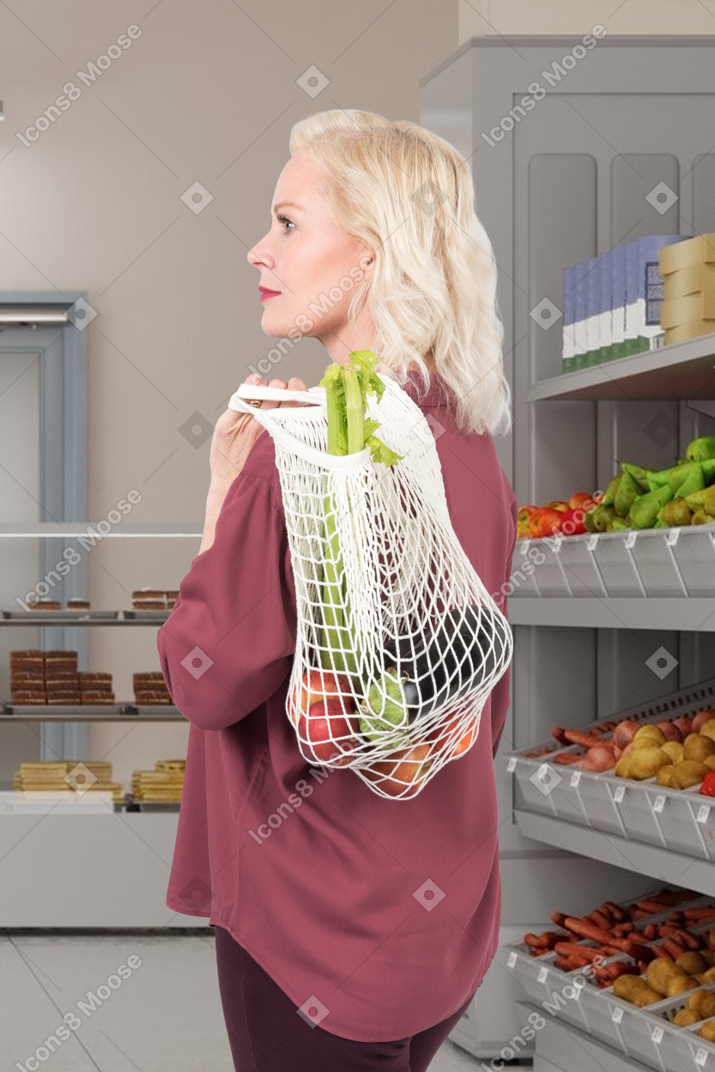 A woman holding a reusable bag with vegetables and fruits  in a grocery store