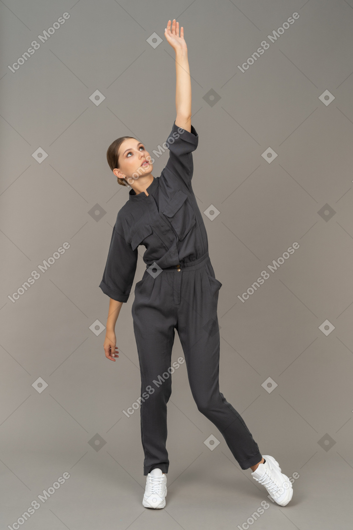 Front view of a young woman in a jumpsuit raising hand