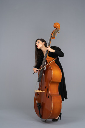 Dreiviertelansicht einer jungen frau im schwarzen kleid, die den kontrabass mit einer schleife spielt