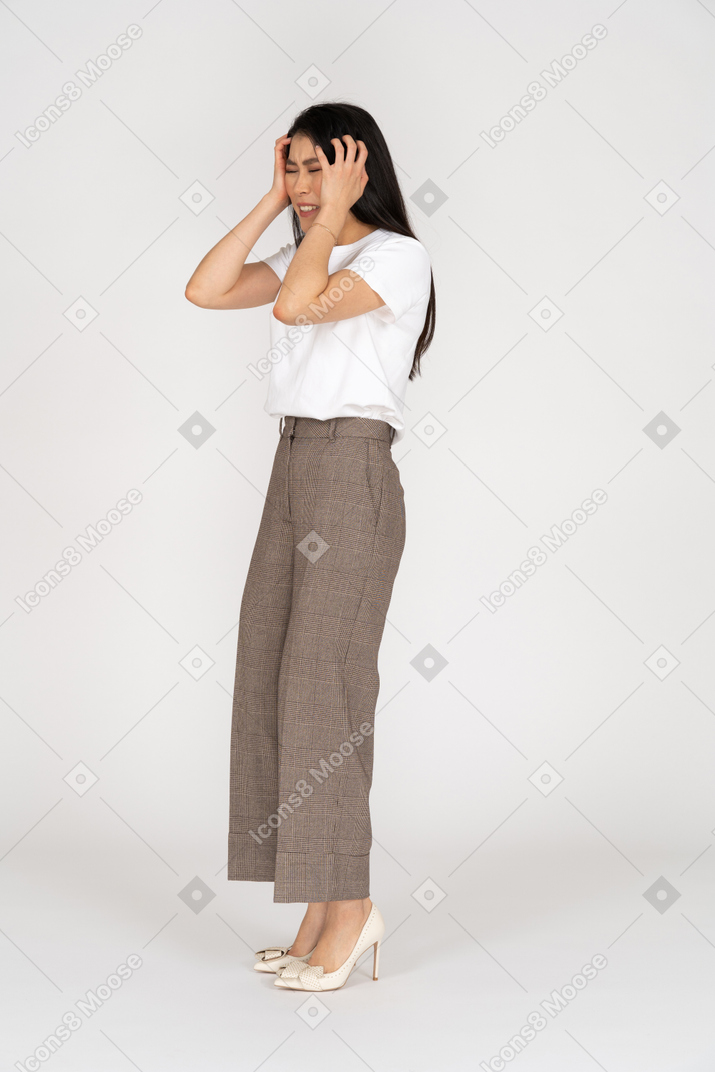 Three-quarter view of a young lady in breeches and t-shirt touching her head