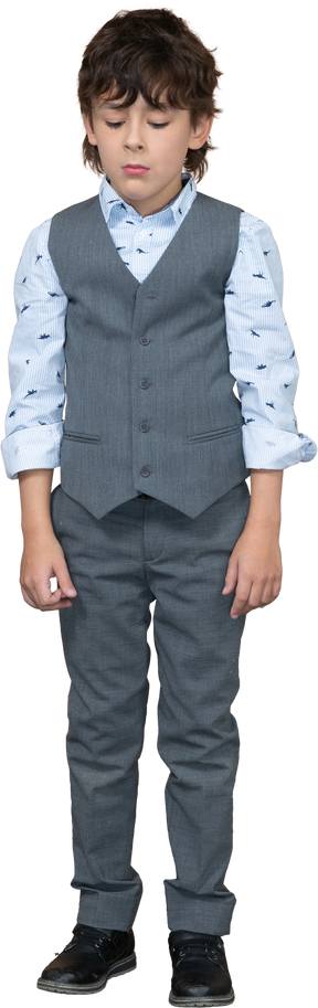 Vista frontal de un niño con traje gris parado y mirando hacia abajo