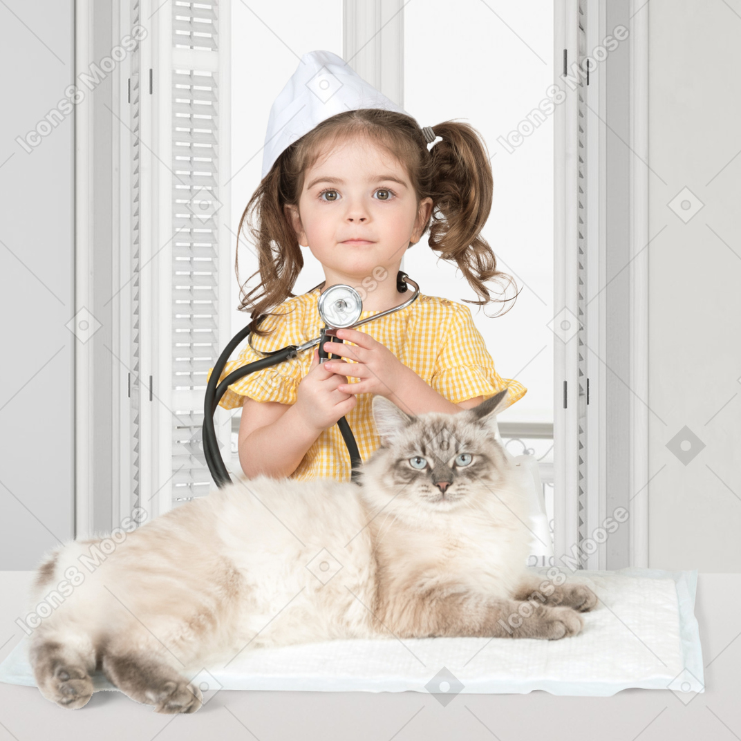 A little girl with a stethoscope standing next to a cat