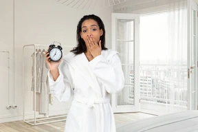 A woman in a bathrobe holding an alarm clock