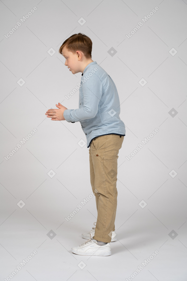 A young boy is standing with his hands together
