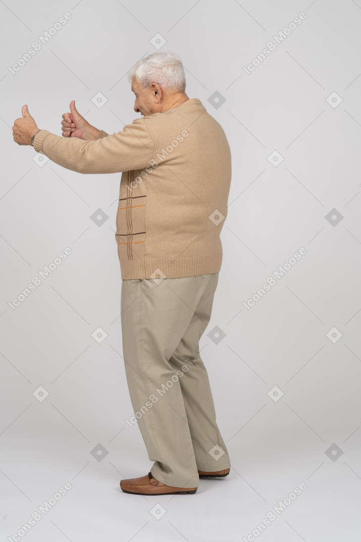 Vista lateral de um velho feliz em roupas casuais, mostrando os polegares