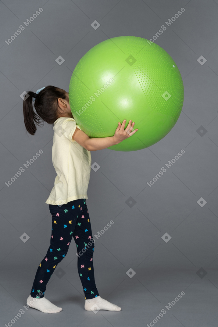 Vista lateral de una niña sosteniendo un fitball verde