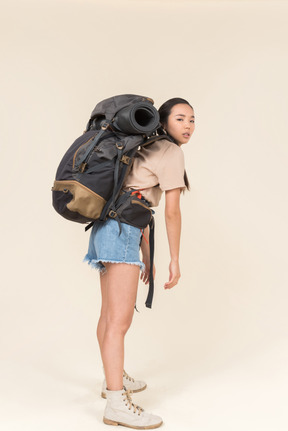 Tired looking female asian hiker standing with huge backpack