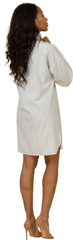 Vista posterior de tres cuartos de una mujer joven de piel oscura con vestido blanco ajustando su cuello