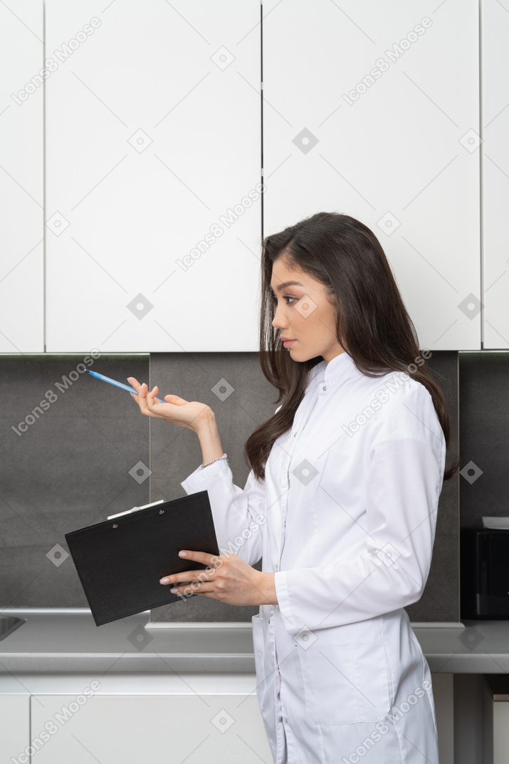 Vista lateral de uma médica questionadora olhando para o lado e segurando uma caneta e um tablet