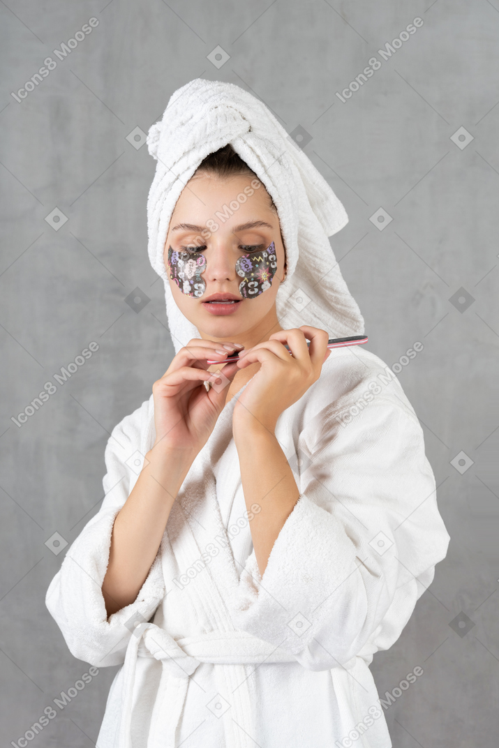 Mujer en bata de baño limandose las uñas
