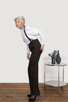 Vista lateral de una anciana en ropa de oficina inclinada hacia adelante mientras toca su trasero