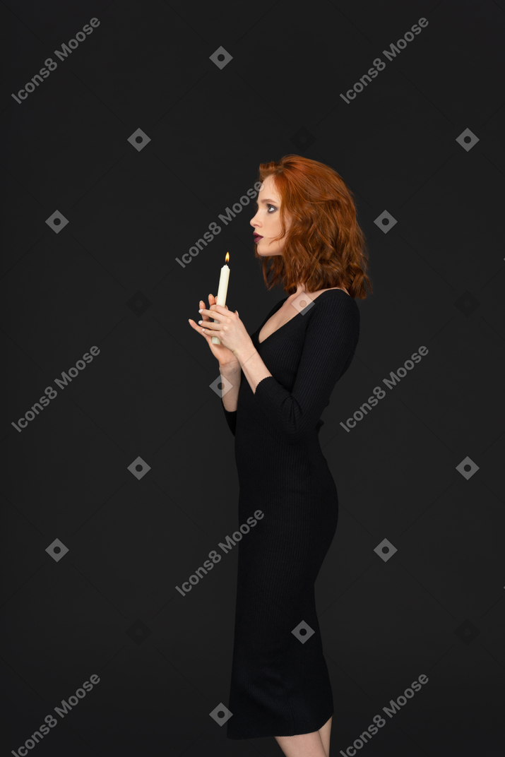 A side view of a sexy girl posing on a dark background and holding a candle