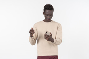 Junger schwarzer mann in einem grauen pullover mit seinem smartphone