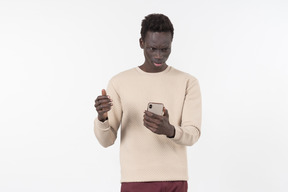 Young black man in a grey sweater using his smartphone