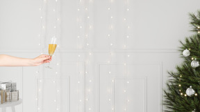 Mão segurando uma taça de champanhe no pano de fundo das luzes de natal