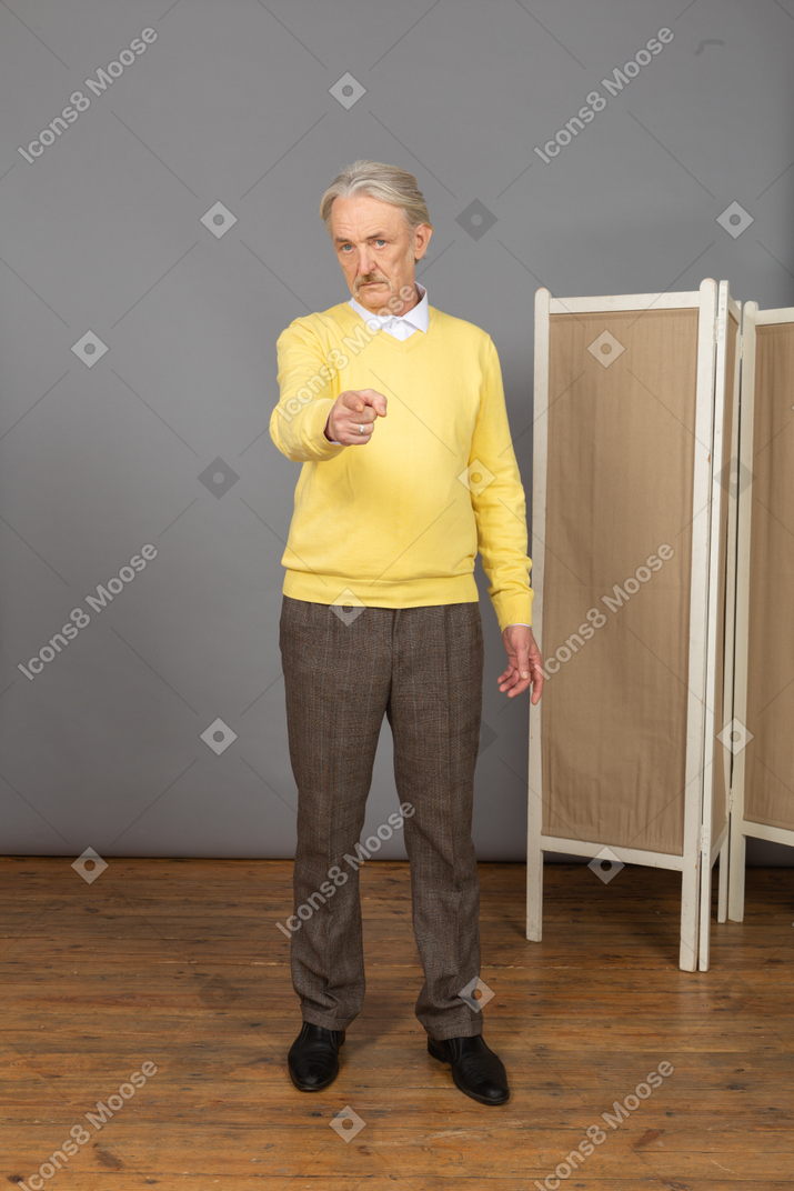 Vista frontale di un vecchio uomo che punta il dito mentre guarda la fotocamera