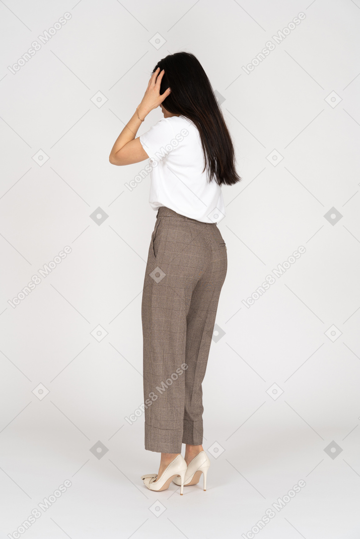 Three-quarter back view of a young lady in breeches and t-shirt touching her head