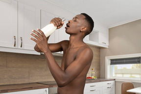 A man drinking from a bottle in a kitchen