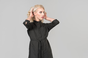 A young blond-haired person in a black dress  standing against the plain grey background