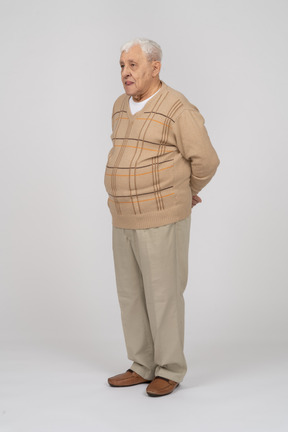 Front view of an old man in casual clothes standing with hands behind back