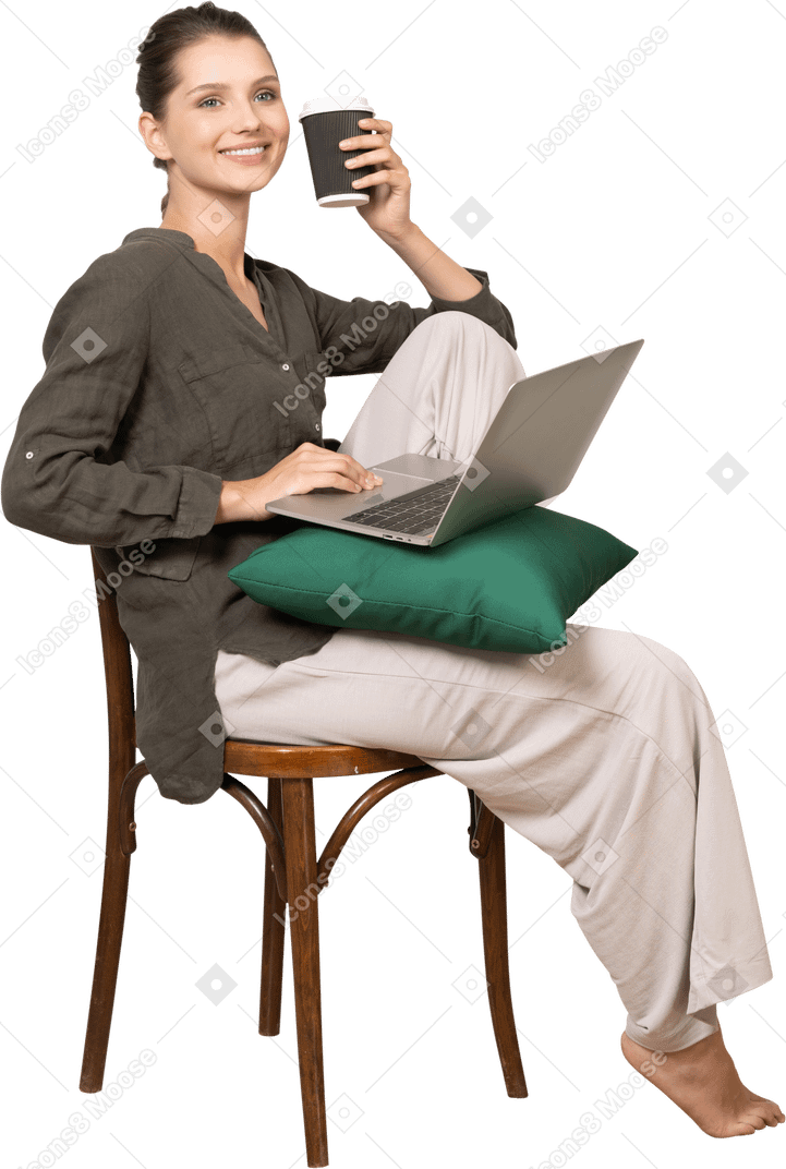 一个微笑的年轻女子坐在椅子上，拿着她的笔记本电脑和咖啡杯的四分之三视图