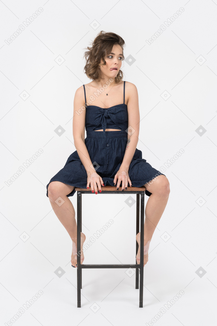 Displeased woman sitting on bar stool with her legs spread apart