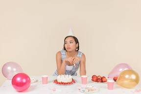 Грустная молодая азиатская женщина сидит за столом на день рождения