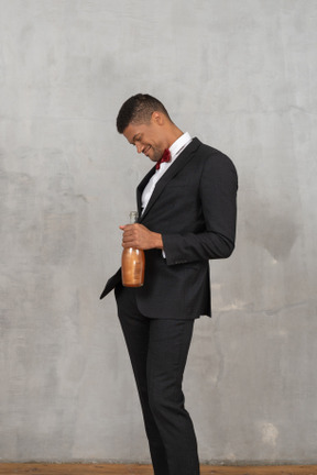 Smiling young man holding a liquor bottle and looking down