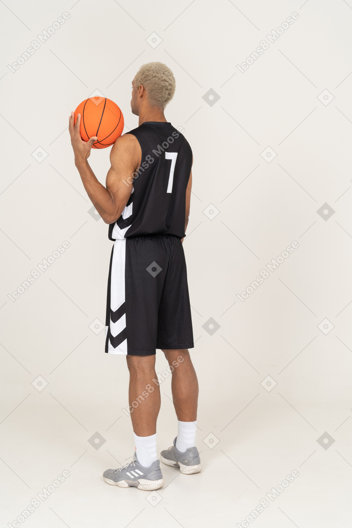 Vista traseira a três quartos de um jovem jogador de basquete segurando uma bola