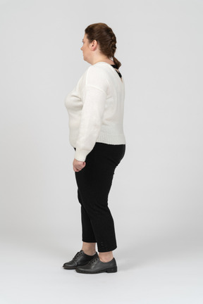 Plus size woman in white sweater standing in profile