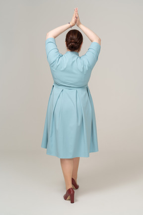 Rear view of a woman in blue dress posing with hands over head