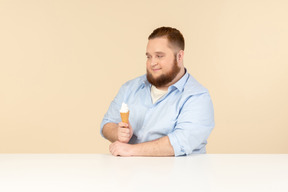 Большой человек сидит за столом и держит мороженое