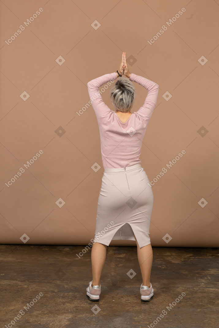 Retrovisor de uma mulher com roupas casuais posando de costas para a câmera com as mãos acima da cabeça
