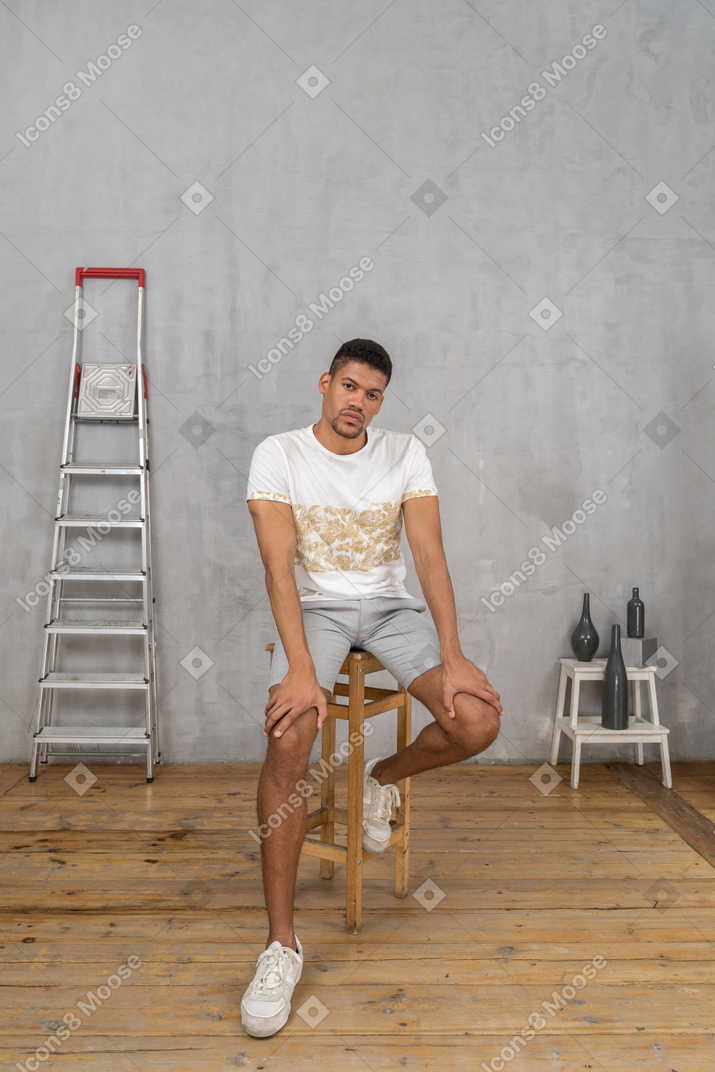 Young man sitting with hands on knees and looking at camera
