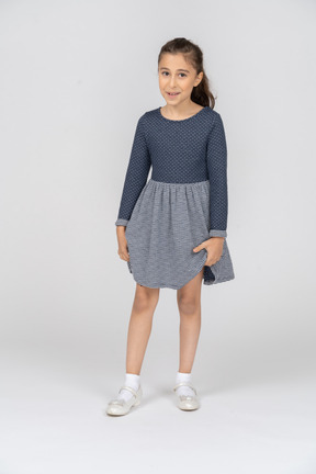 Vista frontal de una niña sosteniendo el dobladillo de su falda con una leve sonrisa
