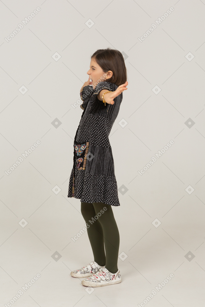 Маленькая девочка в платье, растягивая спину и руки, вид сбоку