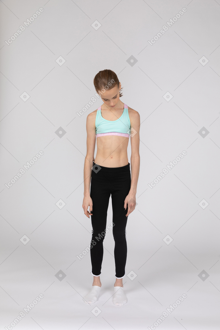 Vista frontal de una jovencita en ropa deportiva inclinando la cabeza hacia abajo