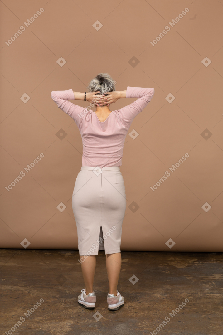 一个穿着休闲服的女人双手放在脑后站立的后视图