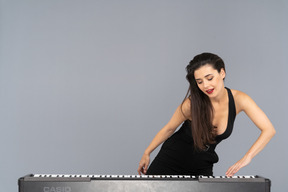 Vista frontal de uma jovem de vestido preto colocando a mão no teclado e inclinando-se para o lado