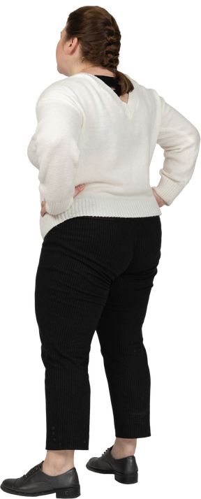 Rear view of a plump woman in casual clothes standing with hands on hips