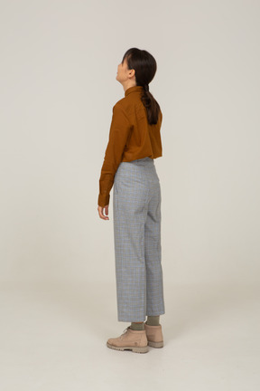 Vista posteriore di tre quarti di una giovane donna asiatica in calzoni e camicetta che guarda in alto