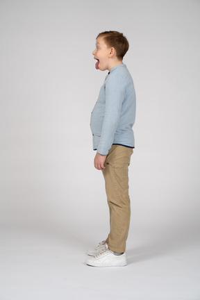 Vista lateral de um menino bonito em roupas casuais, mostrando a língua