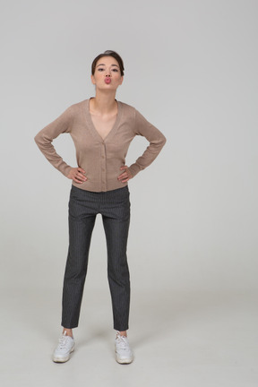 Front view of a young lady in pullover and pants sending an air kiss and putting hands on hips