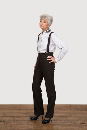 Three-quarter view of a displeased old lady in office clothing putting hands on hips